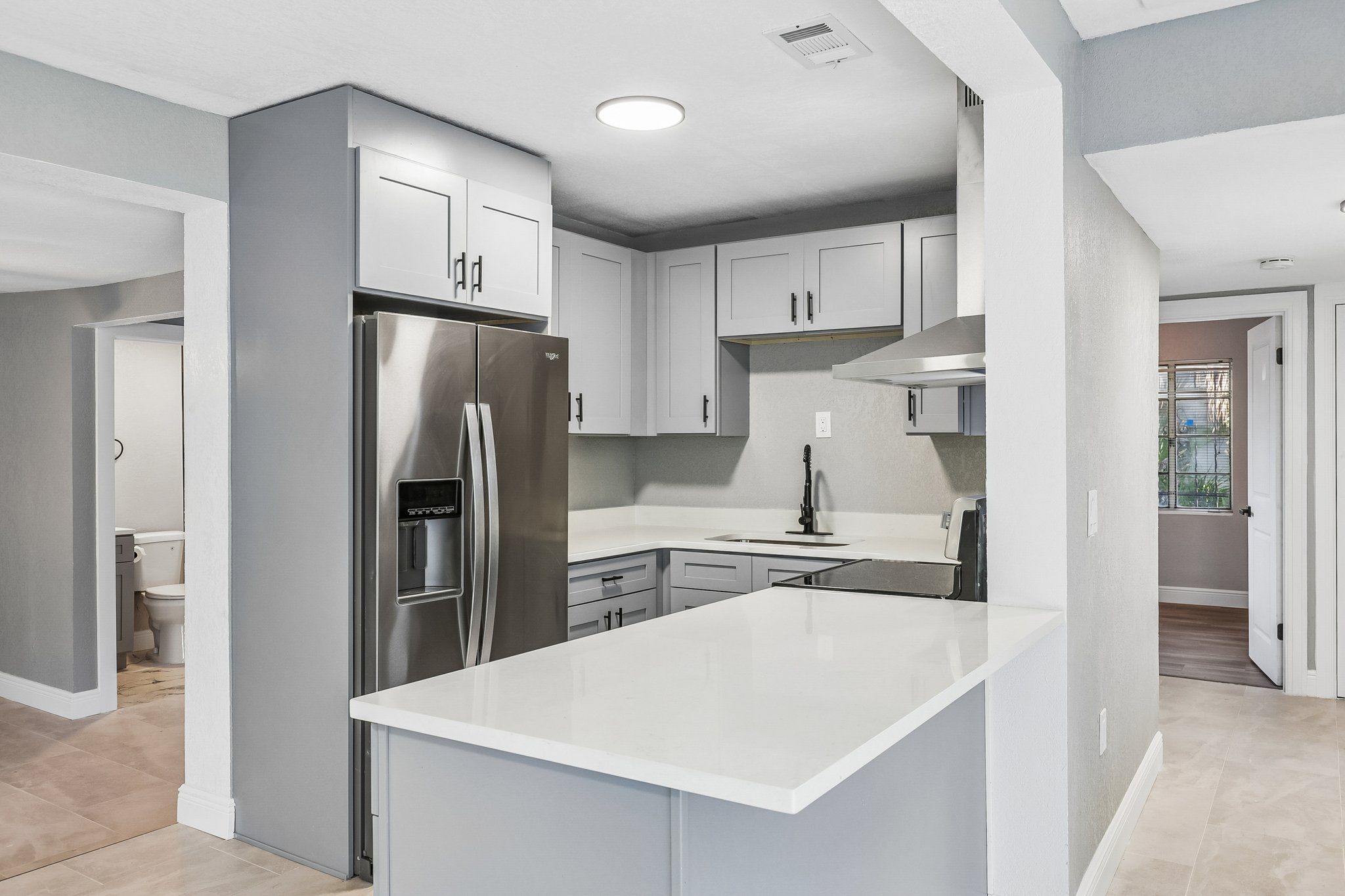Remodeled kitchen with gray shaker cabinets, white quartz island and stainless refrigerator at 2217 Mallory Ave, Tampa