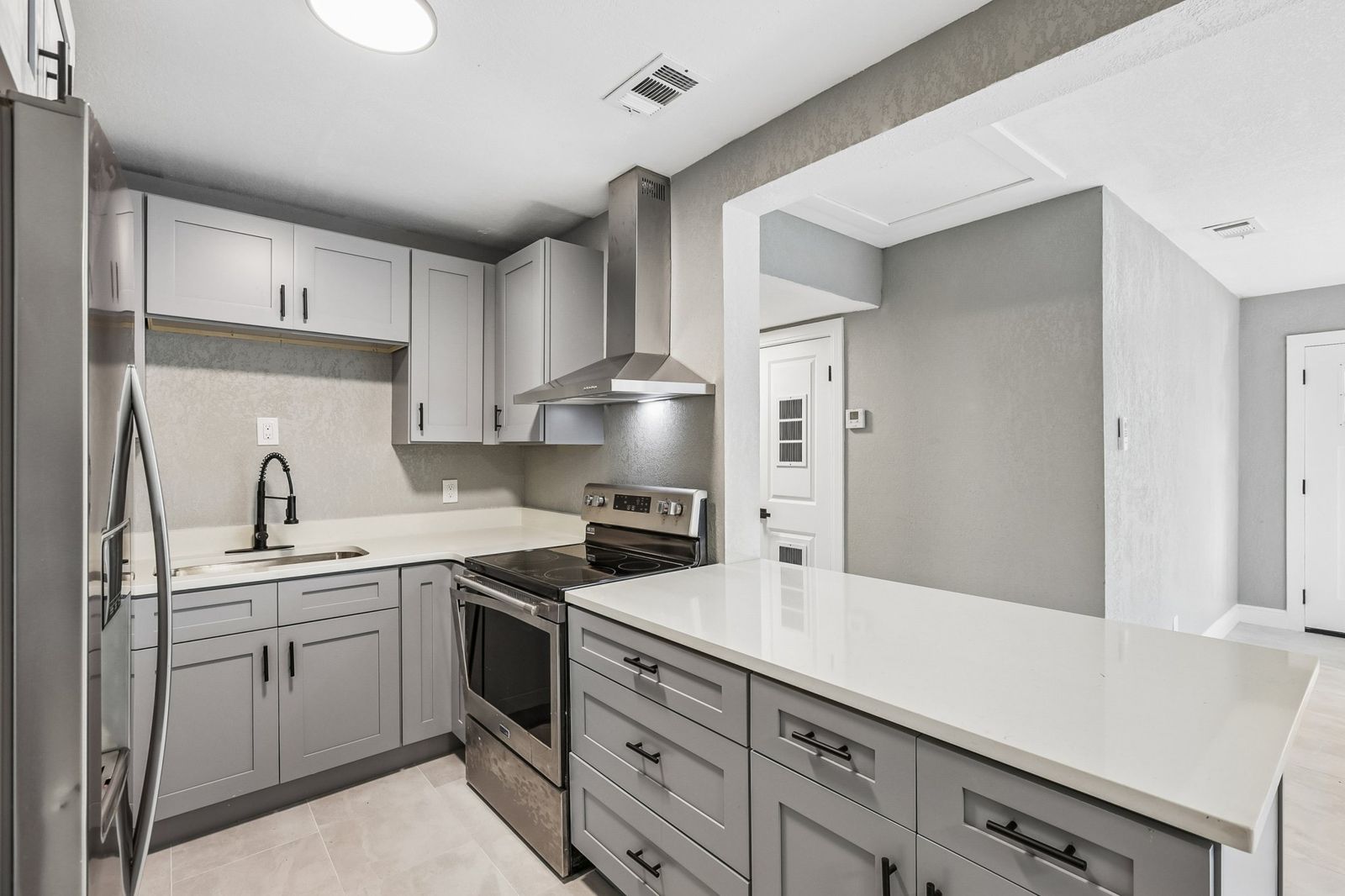 Renovated kitchen with gray shaker cabinets, white quartz counters and stainless appliances